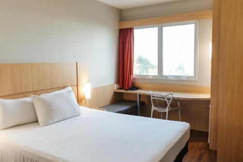 a bedroom with a bed and a desk and a window at Aéra São José Floripa in São José