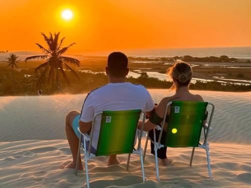 a couple sitting in chairs on the beach watching the sunset at Pousada Zona do Kite Jeri in Jericoacoara