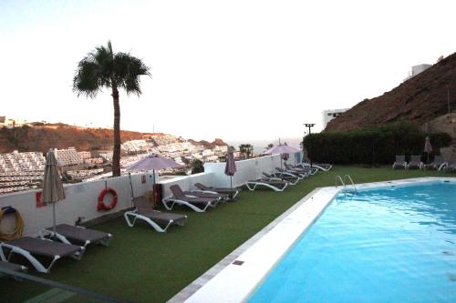 a swimming pool with lounge chairs and a palm tree at OceanEye Apartment with heated pool in Mogán