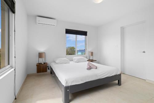a white bedroom with a bed and a window at Playa Breeze Apartment in Kralendijk