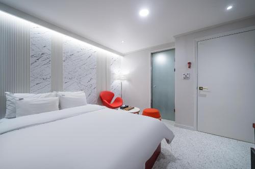 a white bedroom with a bed and a red chair at 넘버25호텔 길동점 in Seoul