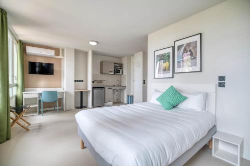 a bedroom with a large white bed and a kitchen at Appart'hôtel Toulouse Zénith in Toulouse