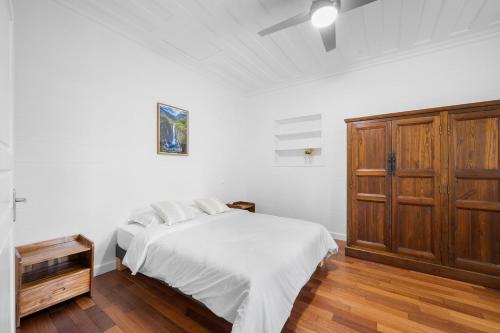a white bedroom with a bed and a wooden cabinet at Domaine Honore - Case Créole dans Jardin Tropical in Sainte-Rose