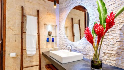 a bathroom with a sink and a vase with red flowers at Tulemar in Manuel Antonio