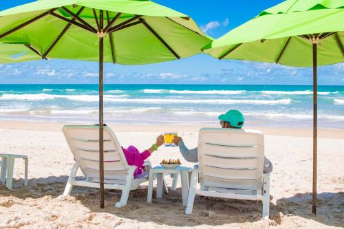 a man sitting in chairs on the beach under an umbrella at Vivá Porto de Galinhas Resort in Porto De Galinhas
