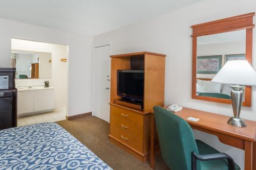 a hotel room with a desk with a television and a bed at Days Inn by Wyndham Fort Myers Springs Resort in Estero