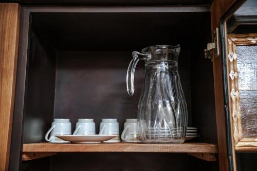 a glass jug sitting on a shelf with cups at Abbi Holidays - Jaffna Luxurious Villa in Jaffna