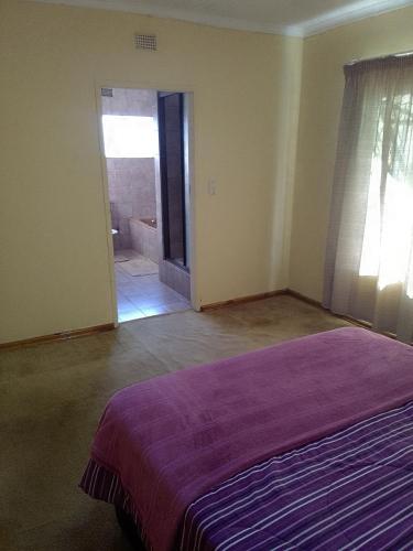 a bedroom with a purple bed and a bathroom at 19 on Smit in Piet Retief