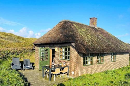 a hut with a grass roof with a table and chairs at 21300-Ulfborg-Somaerkevej-6-b in Vedersø Klit