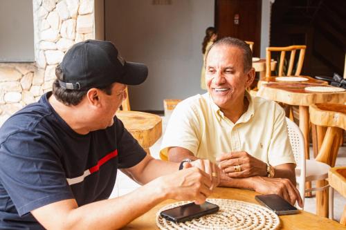 a man sitting at a table talking to another man at Pousada Villa Uçá Frances - Praia do Frances in Marechal Deodoro