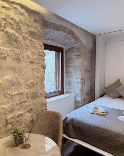 a bedroom with a stone wall with a bed and a table at Casa Del Sol Pietra Kotor in Kotor