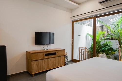 a bedroom with a bed and a flat screen tv at Suksma Guesthouse in Canggu