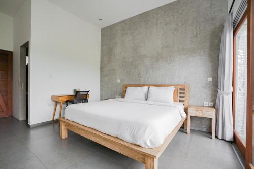 a bedroom with a white bed and a concrete wall at Suksma Guesthouse in Canggu