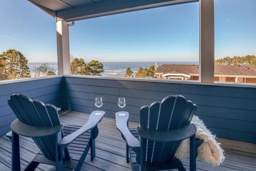 a porch with two chairs and a table with wine glasses at The Moby House Coastal Retreat with Ocean Views & Hot Tub in Depoe Bay