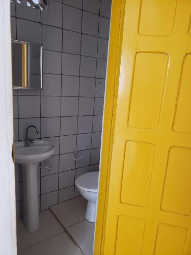 a yellow door in a bathroom with a toilet and sink at Casa Pequena e agradável em Ilhéus in Ilhéus