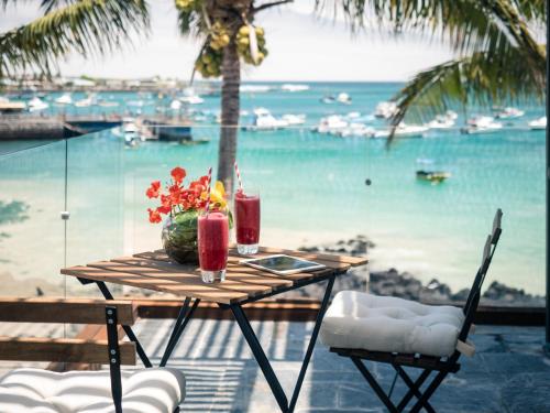 a table with two drinks on a balcony with a view of the ocean at Golden Bay Galapagos in Puerto Baquerizo Moreno