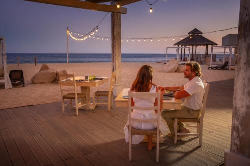 a man and woman sitting at a table on the beach at Sandos Finisterra All Inclusive in Cabo San Lucas