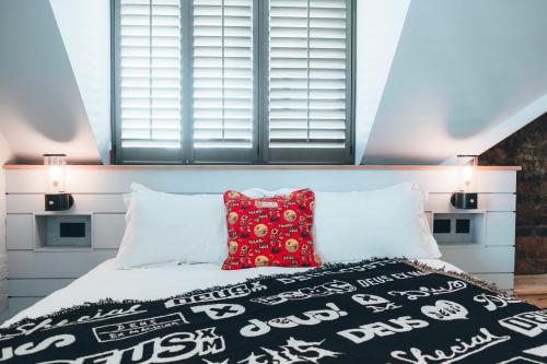 a bedroom with a bed with a red pillow and two windows at Deus Ex Machina Hotel in Bournemouth