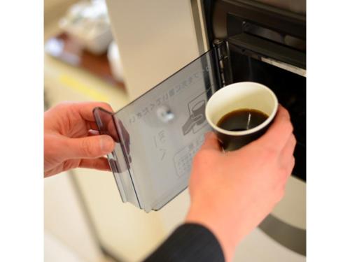 a person is putting a cup of coffee in an oven at Smile Hotel Sakurambo Higashine - Vacation STAY 92770v in Higashine