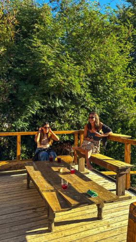 three women sitting around a wooden table on a deck at Alaska Patagonia Hostel in San Carlos de Bariloche