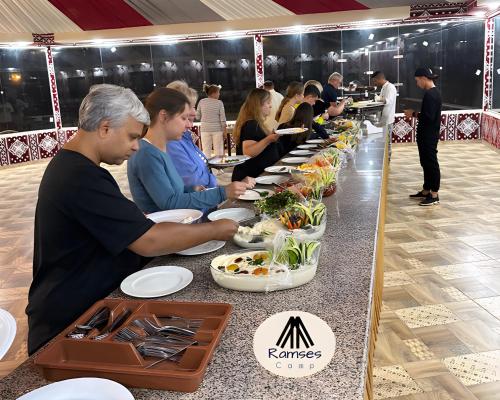 a group of people sitting at a buffet line with plates of food at Ramses luxury rum camp in Wadi Rum