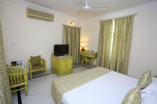 a bedroom with a bed and a tv and a desk at Garden Hotel - Heritage by HRH Group of Hotels in Udaipur