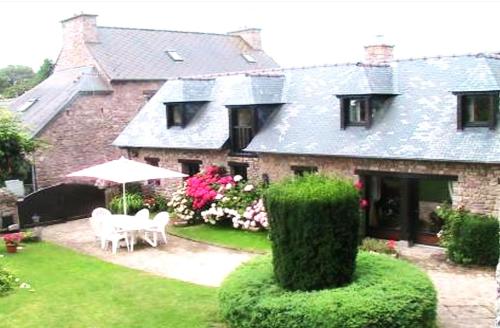 a house with two chairs and an umbrella in the yard at Gîte De Kerberso in Pléhédel