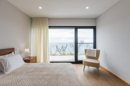 a bedroom with a bed and a chair and a window at Fonte Da Rocha - OCEAN VIEW in Ponta Delgada