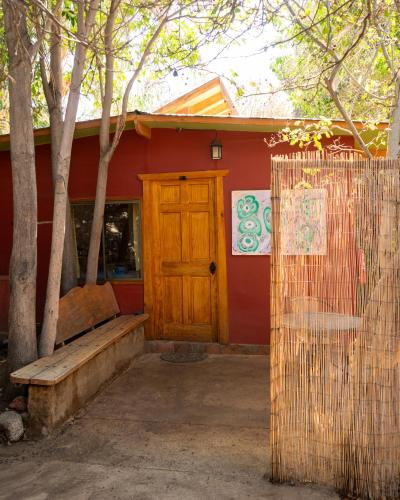 a red building with a wooden door and a bench at El jardín secreto Pisco Elqui in Pisco Elqui