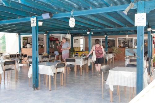 a group of people standing in a restaurant with tables and chairs at Hotel Athinoula in Kefalos