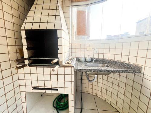 a tiled kitchen with a sink and a window at Onda76 Ap temporada Praia Grande Beira Mar churrasqueira carvão in Praia Grande