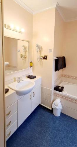 a bathroom with a sink and a mirror and a tub at Parklands Motor Lodge Timaru in Timaru