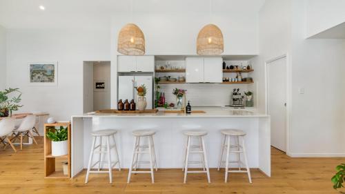 una cucina con bancone bianco e sgabelli da bar di Bangalow Breeze - Lovely Pool - Walk to Centre a Bangalow