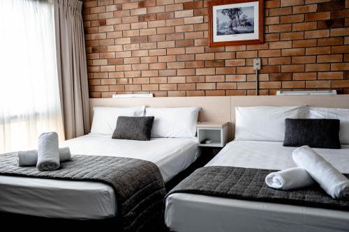 two beds in a room with a brick wall at Buckaroo Motor Inn in Warwick
