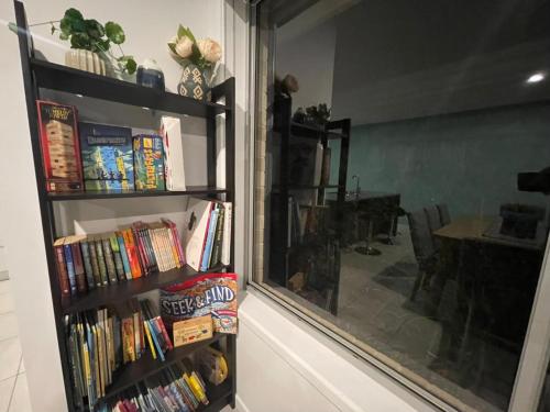 a book shelf filled with books next to a window at Tropical Ocean Vibe Fully Aircon House in Strathpine