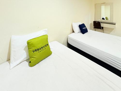 a room with two beds with a green bag on the pillow at Urbanview Hotel Ling near Jawa Timur Park 2 in Tlekung