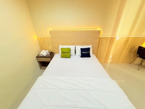 a bedroom with a white bed with two green pillows at Urbanview Hotel Ling near Jawa Timur Park 2 in Tlekung