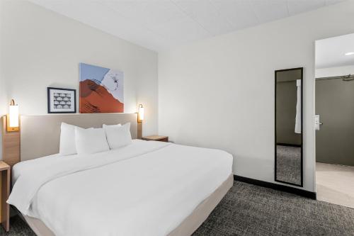 a bedroom with a large white bed and a mirror at Spark by Hilton Des Plaines Chicago O'Hare in Des Plaines