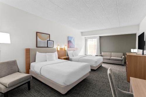 a hotel room with two beds and a chair at Spark by Hilton Des Plaines Chicago O'Hare in Des Plaines
