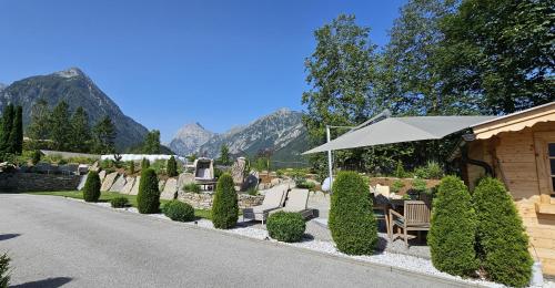 a garden with an umbrella and chairs and trees at Landhaus Achental in Pertisau