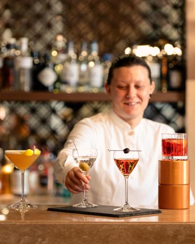 a man standing behind a bar with two cocktails at Aldhafra Desert Resort, Vignette Collection by IHG in Madīnat Zāyid