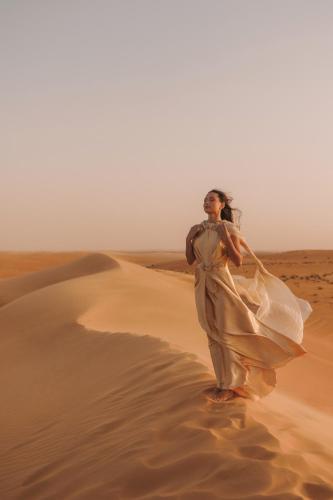 a woman in a dress walking through the desert at Aldhafra Desert Resort, Vignette Collection by IHG in Madīnat Zāyid