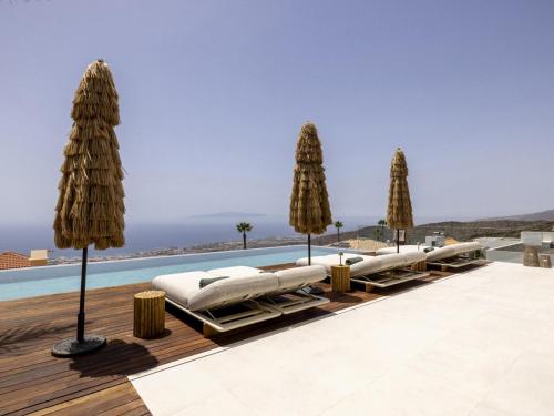a row of chaise lounges with umbrellas and a pool at Villa Kailani in Adeje