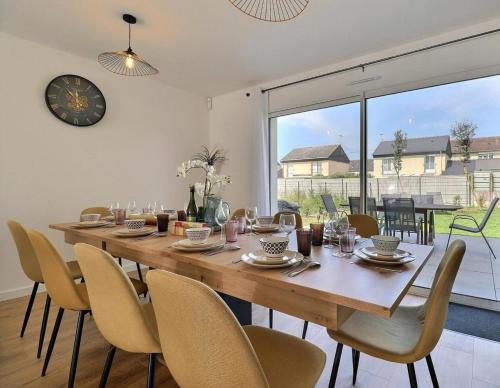 a dining room table with chairs and a clock on the wall at Ker Phan Cozy urban cottage with hot tub in Saint-Aubin-du-Cormier