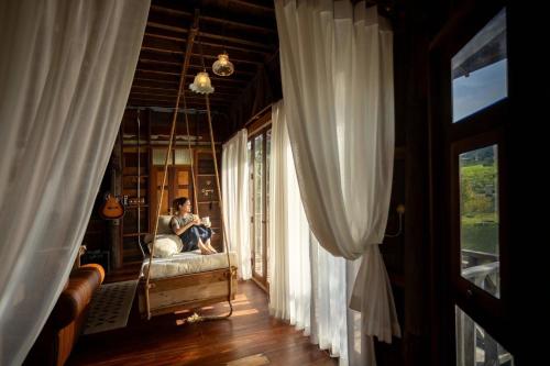 a man sitting on a bed in a room with windows at Luxury Treehouse Khaoyai in Ban Nong Makha