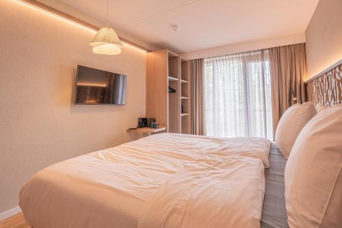 a bedroom with a large white bed with a window at Strandhotel Duinoord in Vrouwenpolder