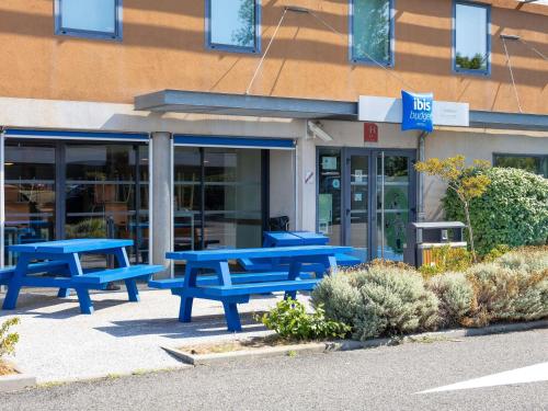 un gruppo di tavoli da picnic blu di fronte a un edificio di ibis budget Toulouse Aeroport a Blagnac
