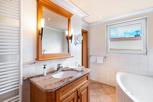 a bathroom with a sink and a mirror and a tub at Wein- und Klimahotel Bergfriedel in Bühlertal