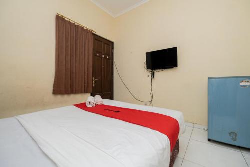 a bedroom with a bed with a red blanket and a television at RedDoorz At Graha 99 Simomulyo in Surabaya