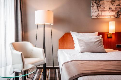 a bedroom with a bed and a chair and a lamp at Leonardo Hotel Aachen in Aachen